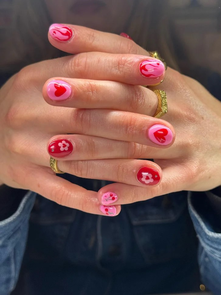 Le mani di una donna intrecciate, con una manicure BIAB rosa acceso e rosso con nail art