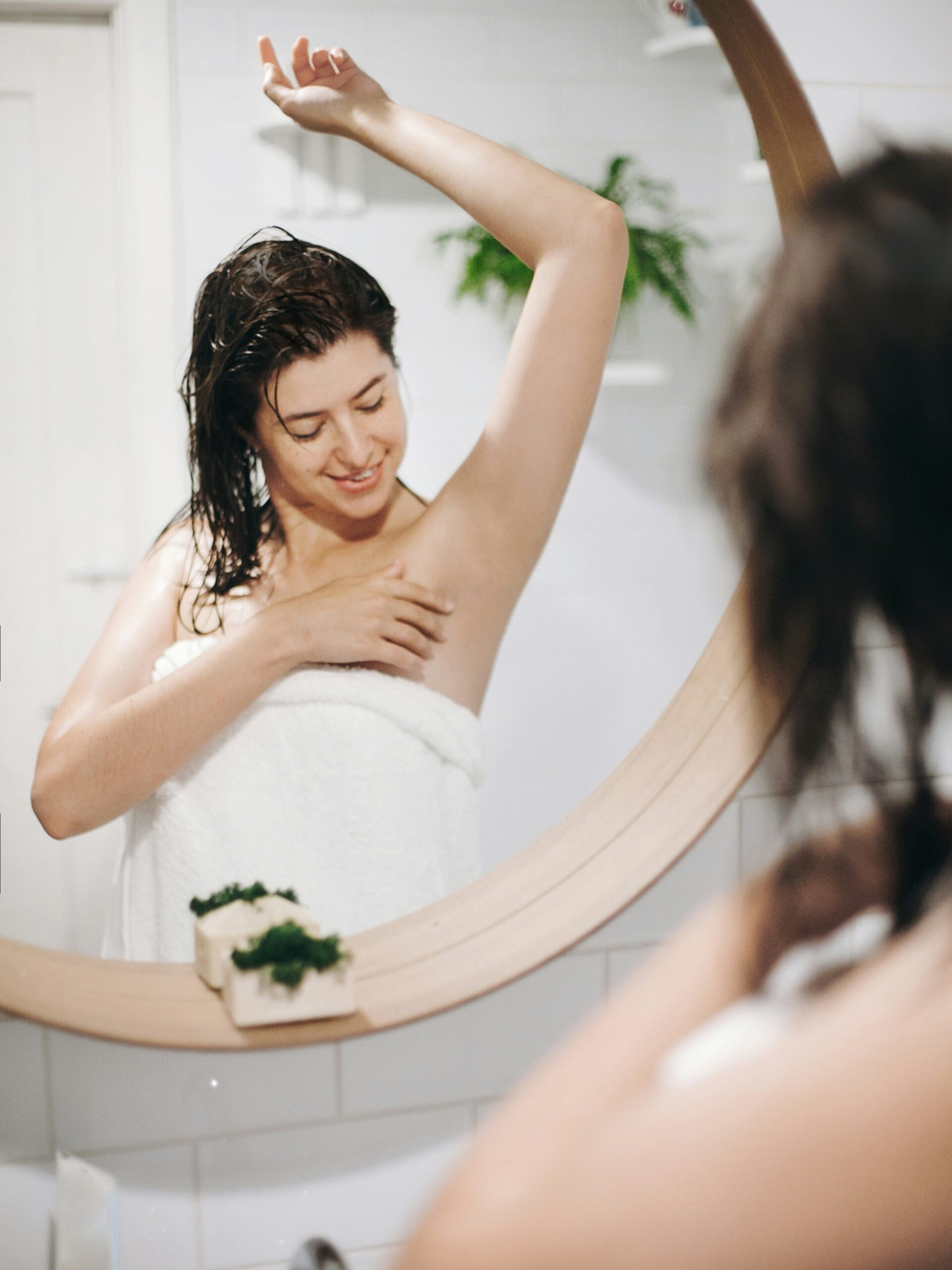 Donna avvolta in un asciugamano da bagno che ammira le ascelle lisce allo specchio dopo un trattamento di luce pulsata
