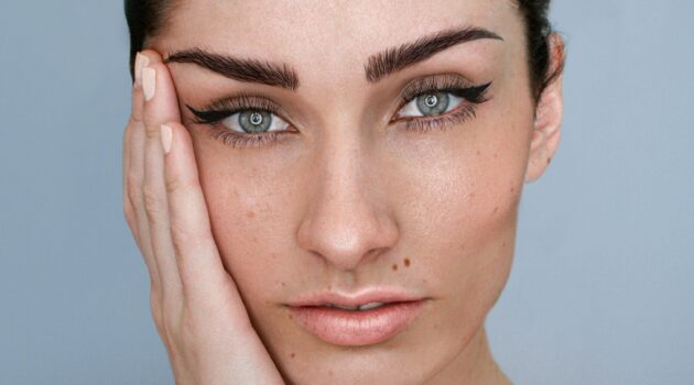 Primo piano del viso di una donna con microblading sulle sopracciglia, trucco naturale e capelli scuri raccolti