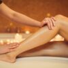 Vista laterale delle mani di un'estetista che accarezzano delicatamente le gambe di una donna distesa su un lettino in un centro estetico dopo una ceretta