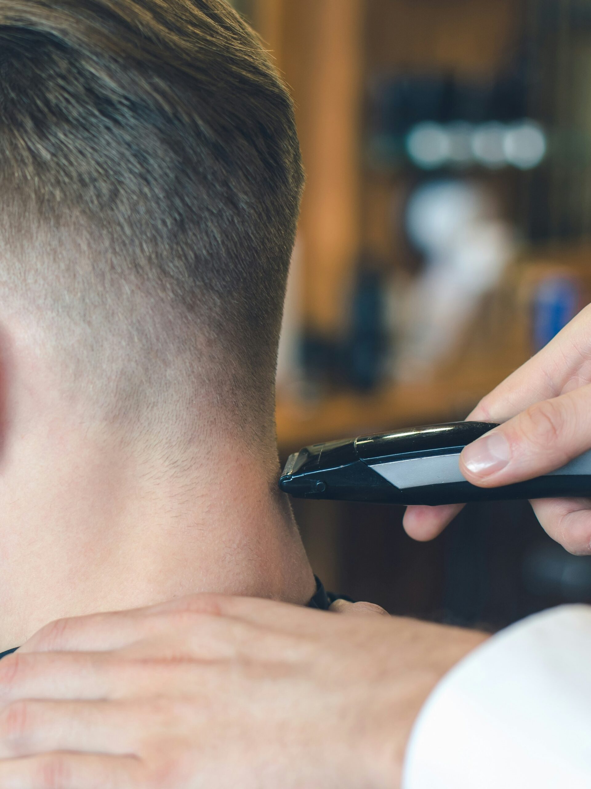 Primo piano di un barbiere che esegue un taper fade con il tagliacapelli sulla parte posteriore della testa di un cliente con capelli lisci