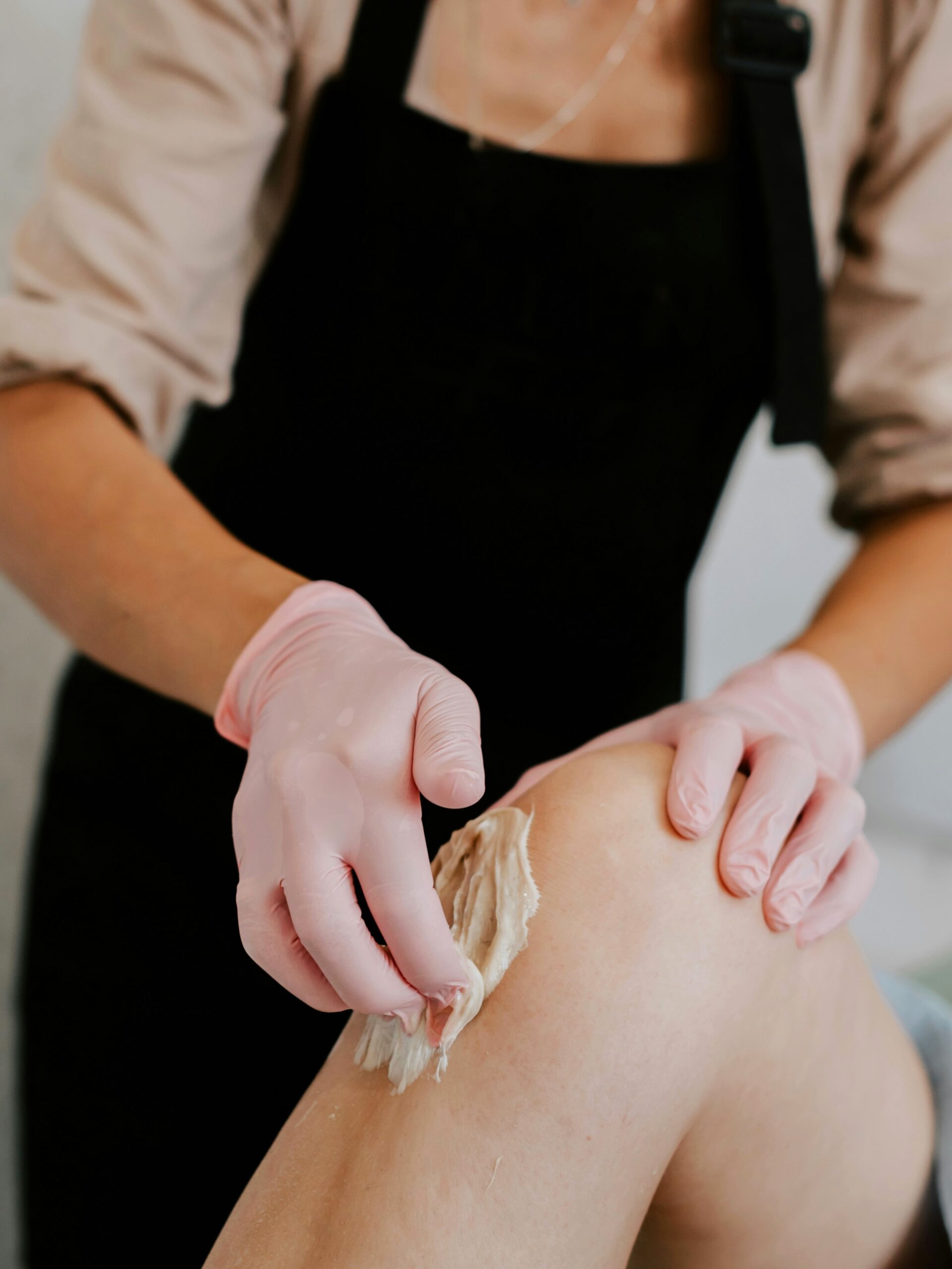 Vista laterale di un’estetista che applica la cera sulla gamba di una cliente distesa comodamente sul lettino in salone