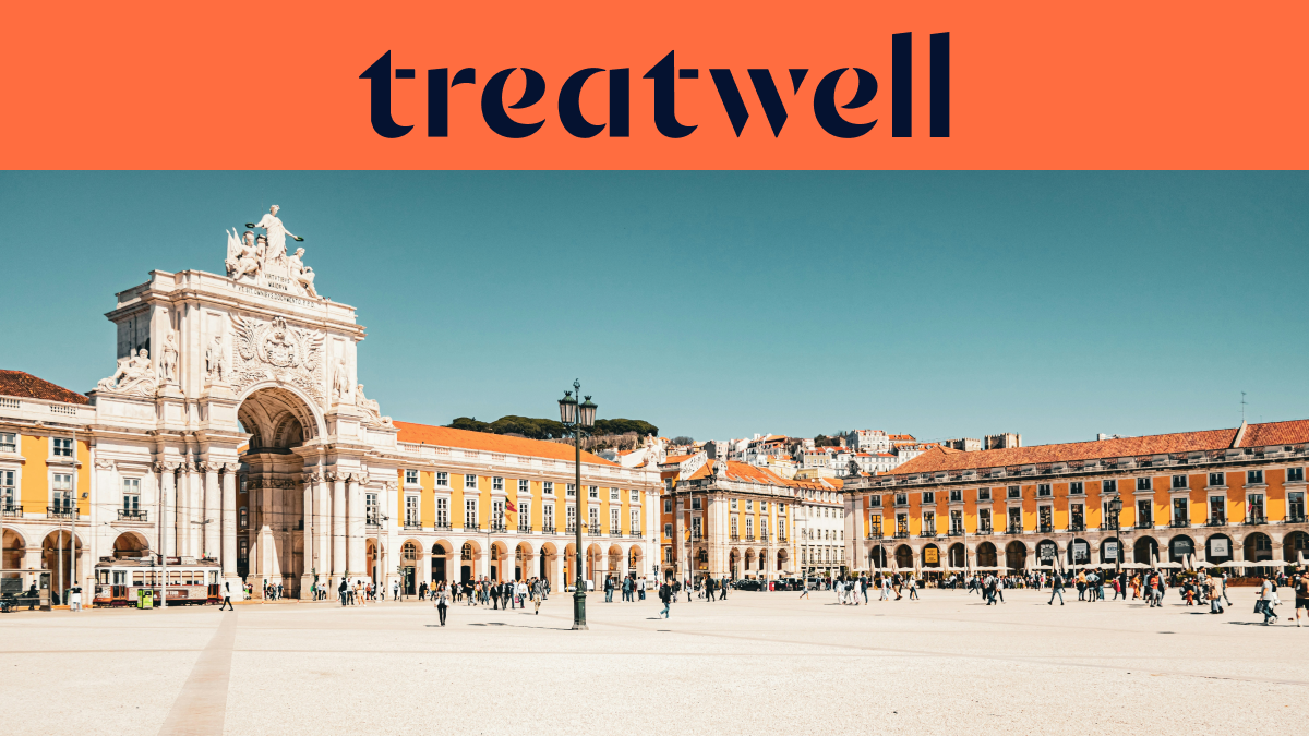 Un banner largo con il logo Treatwell in blu scuro su sfondo arancione nella parte superiore. Sotto il logo, una fotografia luminosa e soleggiata della grande Praça do Comércio a Lisbona, con l'Arco di Rua Augusta bianco, gli edifici gialli con portici ad arco e persone che passeggiano sull'ampia piazza pedonale sotto un cielo azzurro limpido.