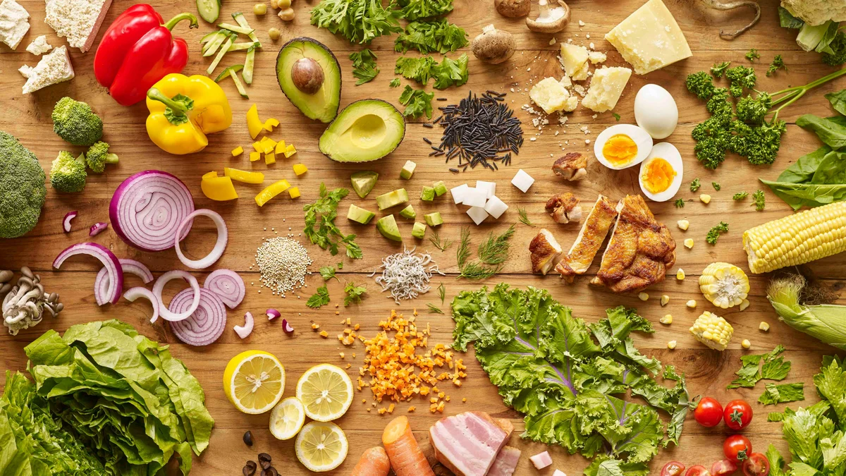 Vista dall'alto di un piano di lavoro in legno coperto di cibo nutriente colorato: uova, verdure, insalata e pollo