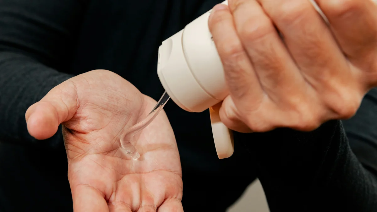 Primo piano delle mani di un uomo che con una mano spreme un tubetto bianco di gel idratante nell’altra mano