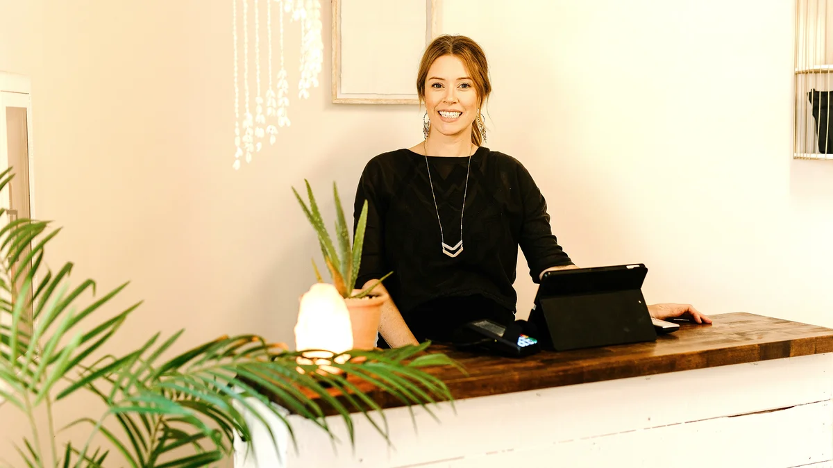 Una donna sorridente è dietro il bancone della reception di un centro estetico