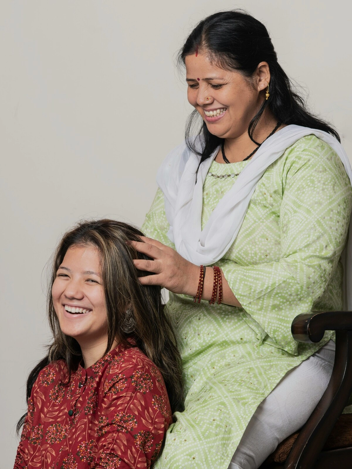 Una donna indiana in abito tradizionale, seduta su una sedia di legno, esegue un massaggio indiano della testa su una donna seduta a terra