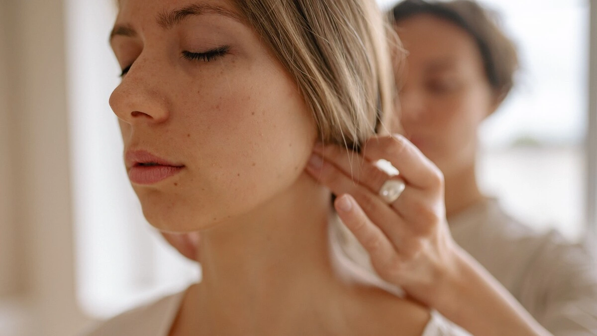Primo piano di una donna con gli occhi chiusi mentre una professionista, durante un massaggio indiano della testa, esercita con le mani una pressione alla base del cranio